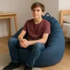 A young boy sits on a large blue beanbag chair in a room with a desk and a bed. Voir les images du produit