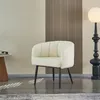 A white fluffy armchair with black legs is shown in a room with a floor lamp and a side table. Produktbild-Vorschau