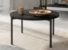 A round black coffee table with a bowl of cookies and a mug on it, placed on a beige rug in a living room setting. Produktbild-Vorschau