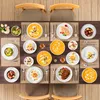 A top-down view of a dining table set for a meal, featuring multiple place settings with plates of food, cutlery, and drinks. Produktbild-Vorschau