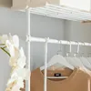 A close-up view of a white telescoping garment rack with several white hangers holding tan sweaters. Produktbild-Vorschau