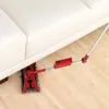 A red cordless sweeper is cleaning under a white sofa. Produktbild-Vorschau