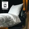 A white Dunlopillo pillow and duvet are arranged on a dark surface, possibly a bed or sofa, with a small candle in a geometric holder in the foreground. Produktbild-Vorschau