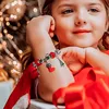 A young girl wearing a Christmas-themed bracelet, with festive lights in the background. Náhľad obrázku produktu
