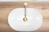 A top-down view of a white oval sink with a gold faucet on a wooden surface. Anteprima dell’immagine prodotto