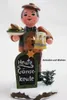 A wooden figurine of a waiter holding a plate of food and a mug of beer, standing in front of a chalkboard sign. Produktbild-Vorschau