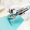 A close-up shot of a white handheld sewing machine stitching a piece of teal fabric. Náhled obrázku produktu