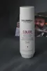 A bottle of Goldwell Dualsenses Color Brilliance Shampoo is placed on a gray surface, with a blurred image of a person in a hat in the background. Produktbild-Vorschau