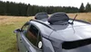 A gray car parked in a grassy field with a forest in the background. The car has two black roof boxes on top. Produktbild-Vorschau