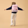 A child wearing a backpack and striped pants, with arms outstretched. Produktbild-Vorschau