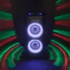 A black trolley speaker with illuminated blue lights on top and purple lights around the speakers, set against a dark background with red and green light effects. Voir les images du produit