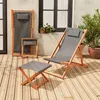 Two wooden deck chairs and a footstool on a wooden deck, with plants and a window in the background. Produktbild-Vorschau