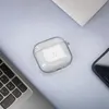 A clear case for Apple AirPods is placed on a light gray surface next to a laptop keyboard and a smartphone. Produktbild-Vorschau