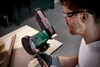 A man is using a belt sander on a wooden surface in a workshop. Produktbild-Vorschau