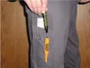 A person's hand is holding a black and yellow marker, with the marker tip inserted into a yellow cap. The marker is partially in a gray pocket of pants, and a white object is also in the pocket. Produktbild-Vorschau