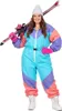 A woman wearing a colorful 80s-style ski suit and a white beanie, holding skis over her shoulder. Produktbild-Vorschau