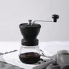 A manual coffee grinder sits on a white wooden board, with coffee beans scattered around it. Náhľad obrázku produktu