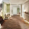 A well-lit hallway with a herringbone wood floor, a bench with cushions, a staircase, and a door. Produktbild-Vorschau
