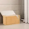 A wicker laundry basket with its lid open, placed on a tiled floor next to a shower curtain. Produktbild-Vorschau