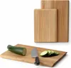 Two wooden cutting boards are shown, with one smaller board placed in front of a larger one. A zucchini and a knife are on the smaller board, with sliced zucchini next to them. Voir les images du produit