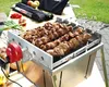 A close-up of a rotating grill with meat skewers cooking, set outdoors on a table with some ingredients and accessories in the background. Produktbild-Vorschau