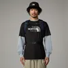 A man wearing a black t-shirt with The North Face logo, a light blue long-sleeved shirt underneath, khaki shorts, a black bucket hat, and a navy blue backpack. Produktbild-Vorschau