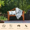 A wooden garden bench with cushions and a blanket is set up in a garden with lush green foliage in the background. Podgląd zdjęcia produktu
