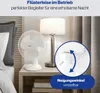 A white table fan is placed on a bedside table next to a lamp and a bed. A close-up inset shows the adjustable tilt mechanism of the fan. Podgląd zdjęcia produktu