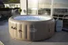 An inflatable hot tub filled with water sits on a patio next to a building with large windows. Produktbild-Vorschau
