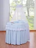 A baby bassinet with a canopy is displayed in front of a window with trees visible outside. Produktbild-Vorschau