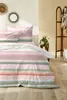A bedroom scene with a bed dressed in pink, green, and white striped bedding. Produktbild-Vorschau