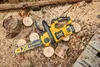 A yellow and black DeWalt cordless chainsaw is placed on a surface covered with sawdust and wood scraps, surrounded by small cut logs. Voir les images du produit