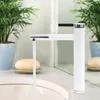 A white faucet with chrome accents is shown in a bathroom setting, with water running into a sink. Two potted plants and bars of soap are visible in the background. Produktbild-Vorschau