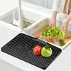 A person is washing fruit in a kitchen sink, with a black drying mat in the foreground holding two apples. Produktbild-Vorschau