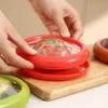 Hands are shown holding and assembling a set of round, lidded food containers, one red and one green, on a wooden cutting board. Another brown container is visible in the background. Produktbild-Vorschau