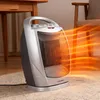 A Kalorik ceramic heater is shown on a rug in a room with wooden furniture and a chair. Orange heat waves emanate from the heater. Podgląd zdjęcia produktu