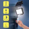A hand holding a remote control, pointing it towards a solar-powered light fixture mounted on a wall. The light fixture has a solar panel and a light emitting panel with multiple LEDs. There are informational graphics on the left side of the image. Produktbild-Vorschau