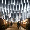 A street decorated with white meteor shower lights for Christmas, with people walking and Christmas trees on display. Produktbild-Vorschau