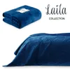 A folded blue blanket is shown in the upper left corner, and a close-up of a blue quilted blanket draped over a bed is shown in the lower portion of the image. Text is present in the upper right corner. Produktbild-Vorschau