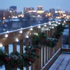 A wooden balcony railing decorated with Christmas garland and lights, with a city skyline in the background. Produktbild-Vorschau