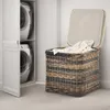 A laundry basket filled with clothes next to a stacked washer and dryer. Produktbild-Vorschau