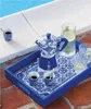 A blue and white patterned tray with a Bialetti Moka pot, two cups of coffee, and two glasses of water with lemon and rosemary, placed on a brick patio next to a swimming pool. Anteprima dell’immagine prodotto