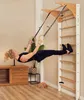 A woman is exercising on a wall-mounted climbing frame with gymnastic rings in a room. Produktbild-Vorschau