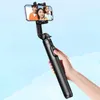 A hand holding a black selfie stick with a phone attached, showing three people smiling in the phone's screen, against a sky background. Náhled obrázku produktu