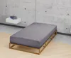A bed frame with a fitted sheet in a minimalist room with a concrete wall. Produktbild-Vorschau