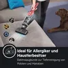 A person is using a red and black cordless vacuum cleaner on a gray sofa, with a brown dog lying on a dark blue rug in the background. Several circular diagrams illustrating allergens are shown on the left side of the image. Produktbild-Vorschau