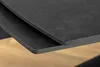 A close-up view of two dark gray tabletops, one slightly overlapping the other, with a light brown wooden floor visible beneath. Produktbild-Vorschau