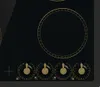 A close-up view of a black glass ceramic hob with gold accents and control knobs. Produktbild-Vorschau