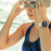 A woman wearing a swimming cap and goggles adjusts her goggles while wearing a smartwatch on her wrist. Voir les images du produit