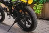 Close-up of the rear wheel and frame of a black electric bicycle, parked outdoors on a paved surface with greenery in the background. Anteprima dell’immagine prodotto